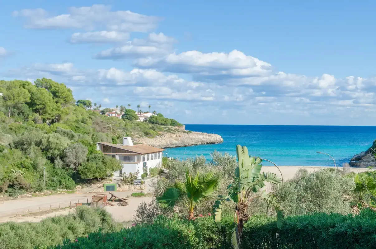 Paisaje costero con una playa de arena, mar turquesa y vegetación.