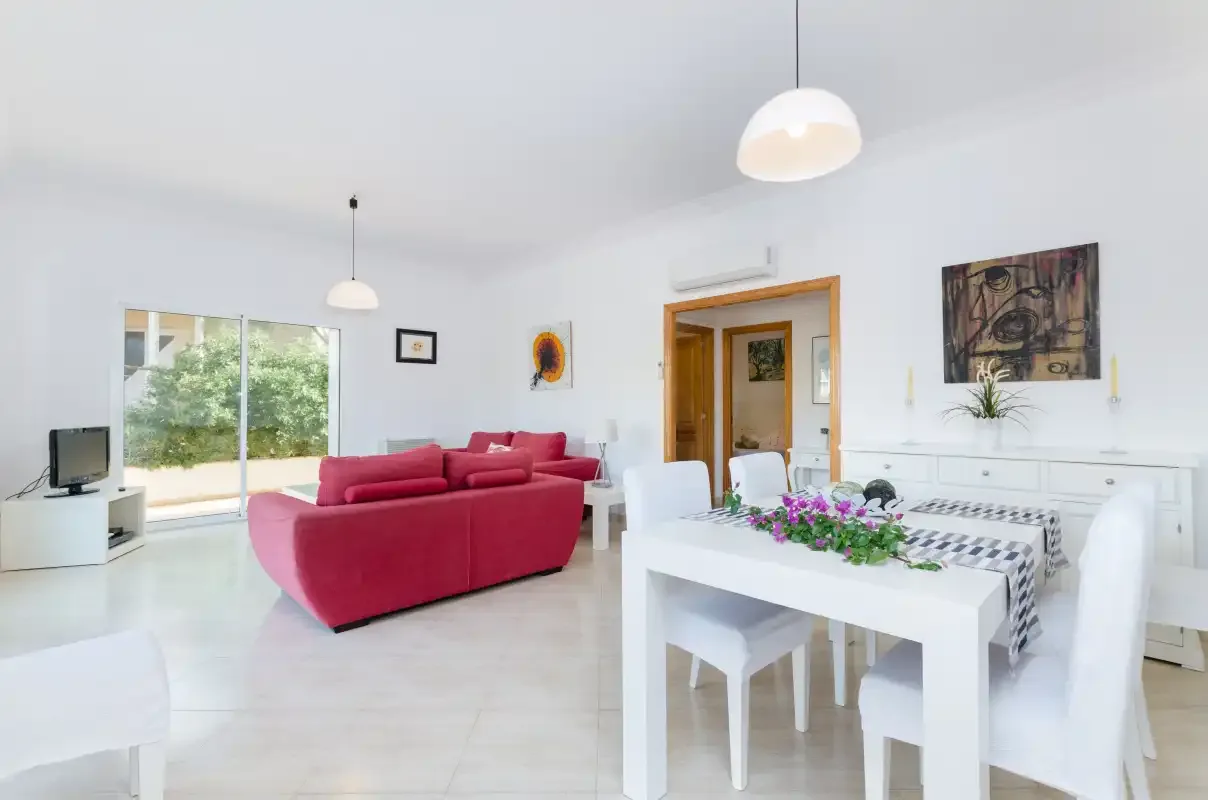 Una luminosa sala de estar y comedor diáfana con un sofá rojo y una mesa blanca.