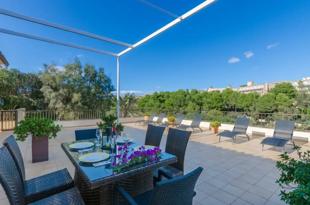 Una terraza soleada al aire libre con mesa, asientos y plantas en macetas.