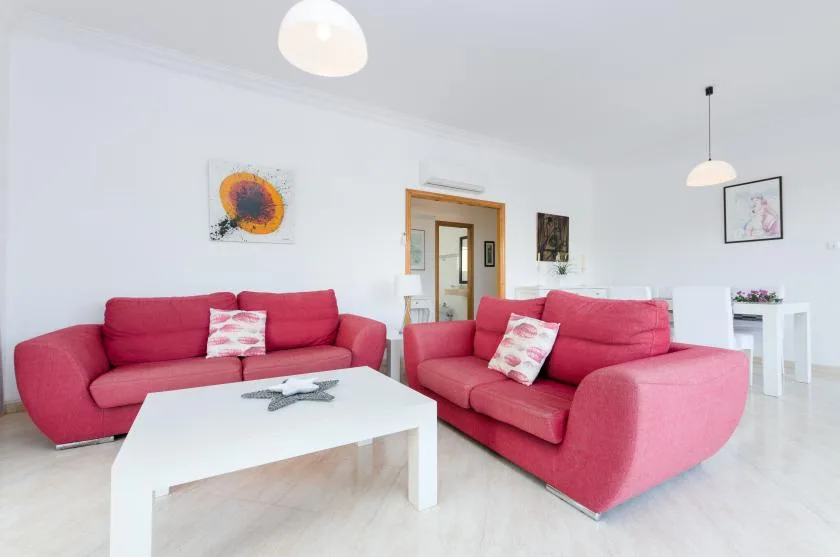 Una sala de estar luminosa con asientos rosas y una mesa de centro blanca.