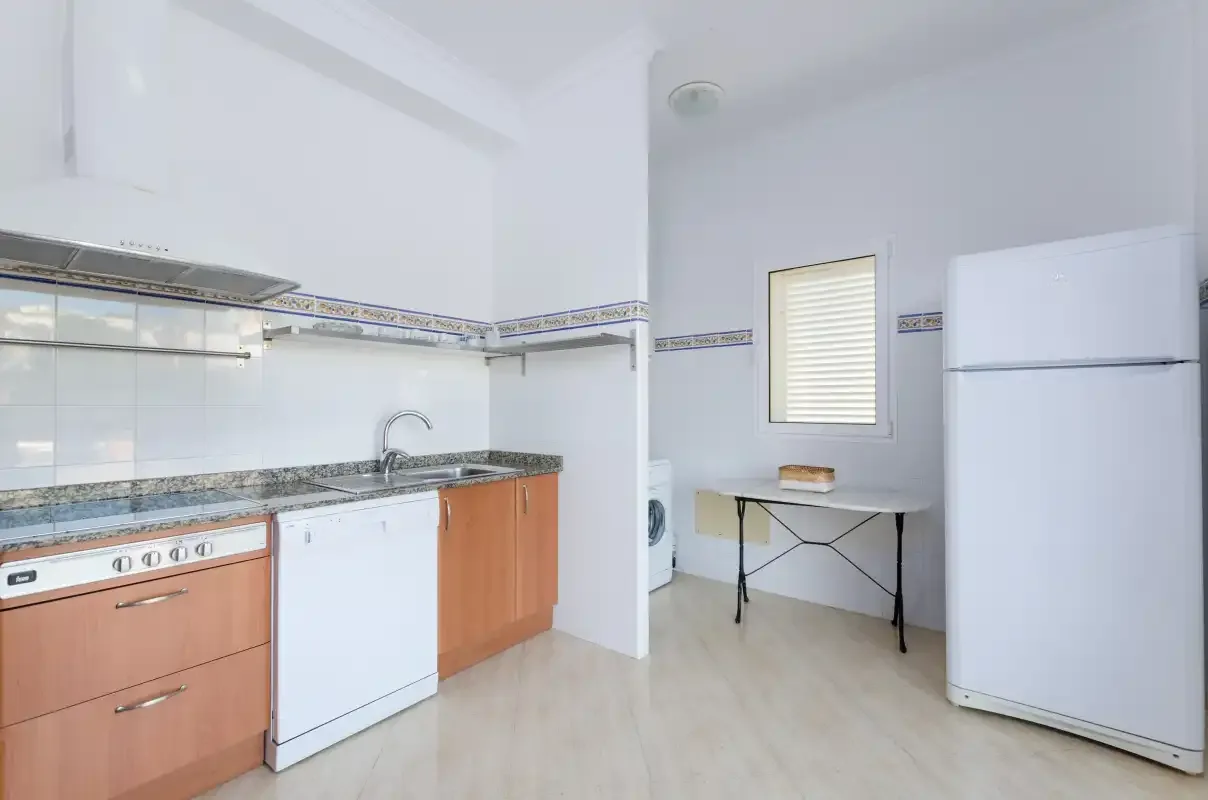Una cocina luminosa con encimeras, armarios, un refrigerador y una mesa pequeña.