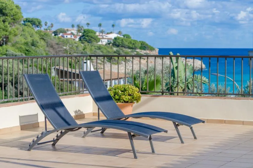Una terraza soleada con tumbonas reclinables da al mar azul.