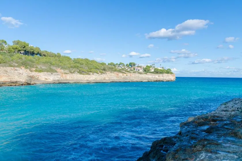 Una costa rocosa bordea aguas azules y claras bajo un cielo luminoso.
