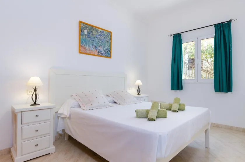 Un dormitorio luminoso con una cama tendida y cortinas turquesas junto a la ventana.