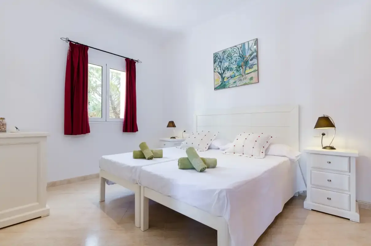 Un dormitorio luminoso con dos camas, cortinas rojas y un cuadro enmarcado.