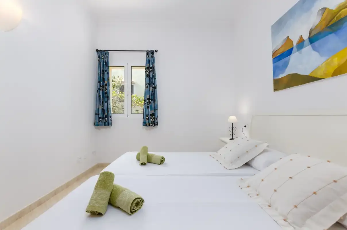 Un dormitorio luminoso con dos camas, cortinas azules y un cuadro de paisaje.