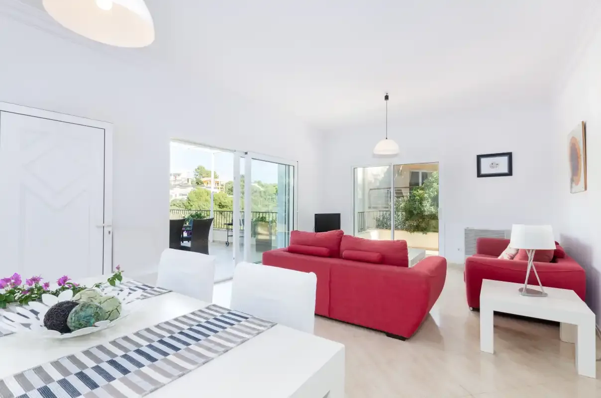 Un salón luminoso con asientos rojos y puertas de vidrio que dan a un patio.