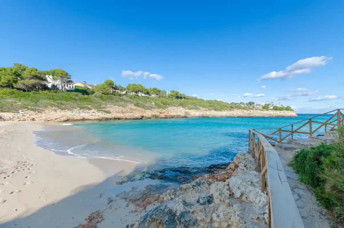 Una pequeña playa de arena se curva junto a aguas azules y una orilla rocosa.