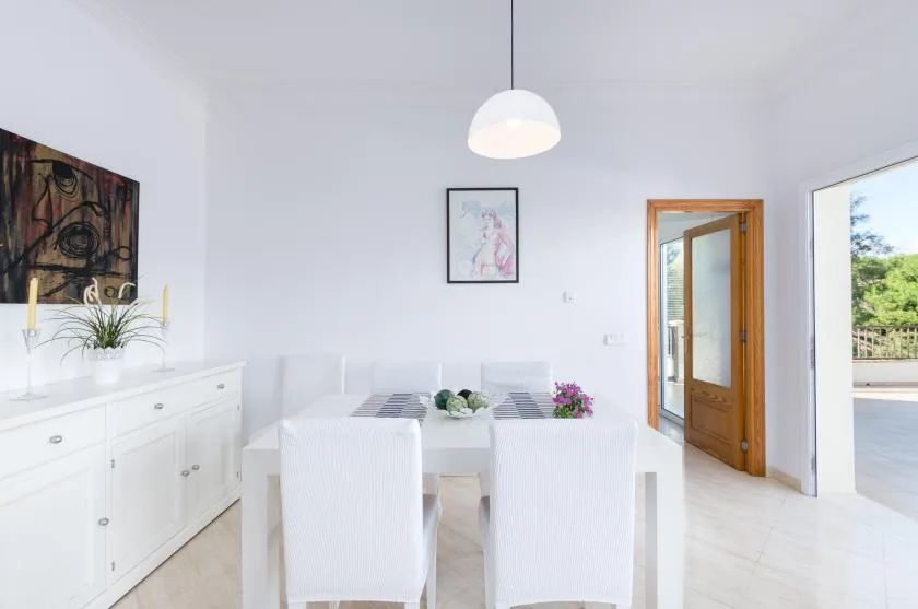 Un comedor luminoso con mesa blanca, asientos y una lámpara colgante.