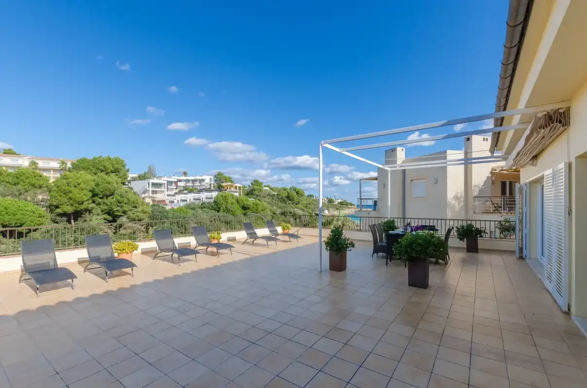 Una amplia terraza embaldosada con asientos al aire libre, plantas en macetas y edificios cercanos.