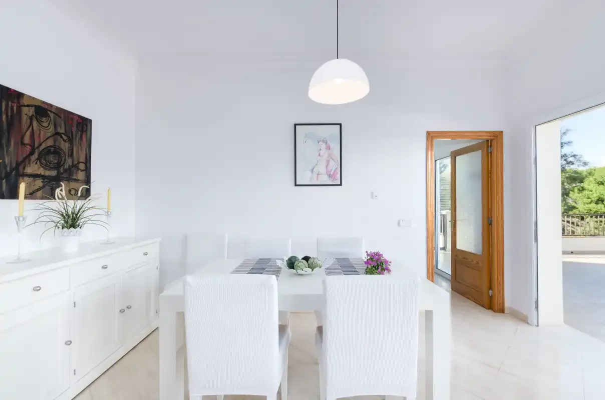 Un comedor luminoso con asientos blancos, una mesa y una puerta abierta.