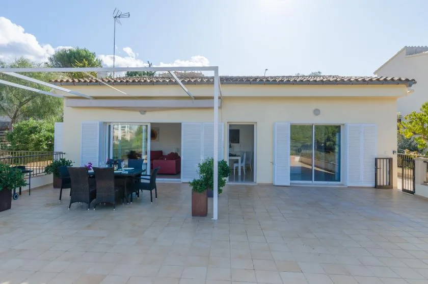 Una terraza exterior de baldosas con una mesa de comedor junto a una casa.