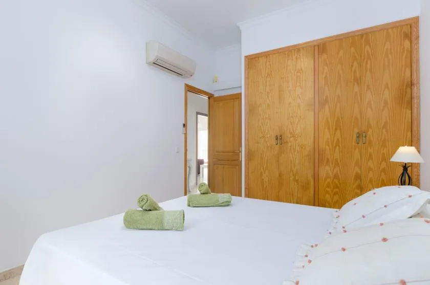 Un dormitorio luminoso con ropa de cama blanca, toallas verdes y armarios de madera.