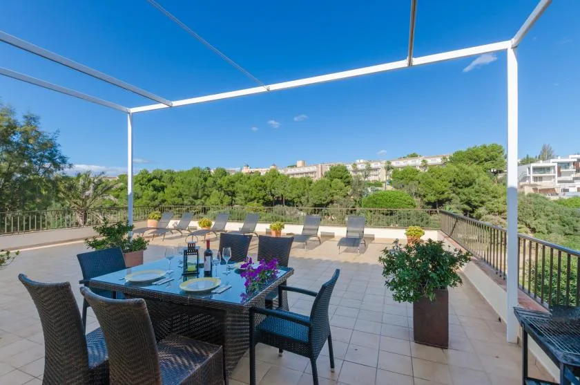 Una terraza en la azotea con asientos al aire libre y una mesa bajo una estructura metálica.