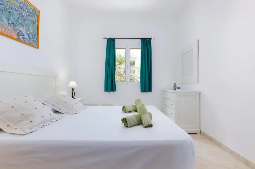 Un dormitorio luminoso con una cama bien arreglada y una ventana enmarcada por cortinas verde azulado.