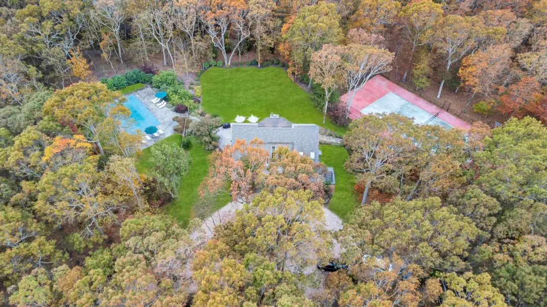 An aerial view of a wooded property with a house, swimming pool, and tennis court.