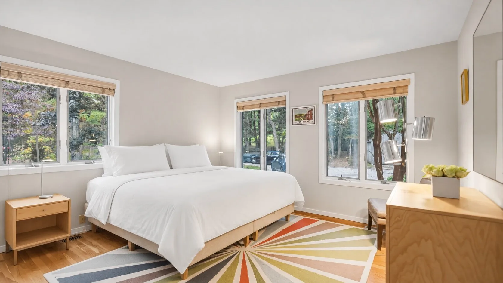 A bright bedroom with a large bed, windows, and a colorful geometric rug.