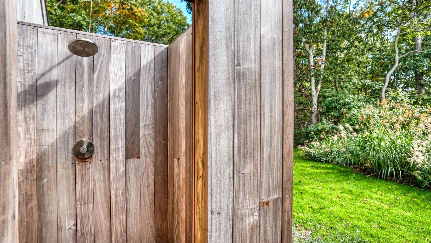 An outdoor shower beside a wooden privacy screen and green garden.