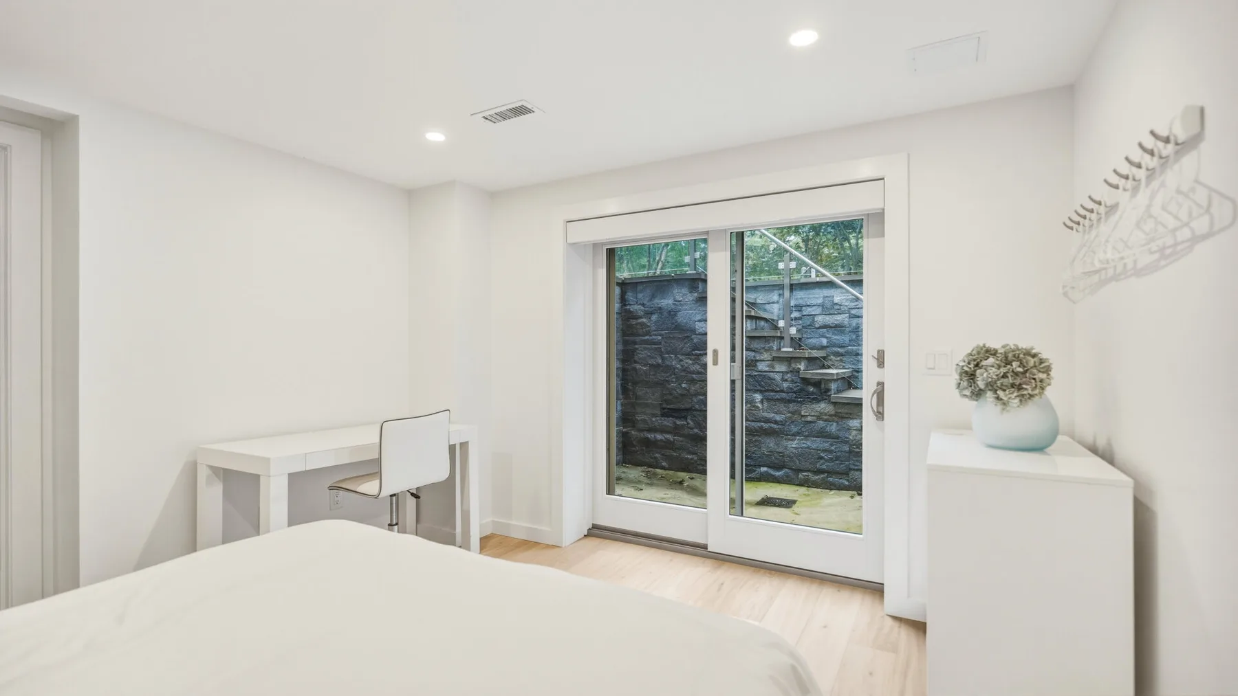 A bright bedroom with a bed, desk, and sliding glass doors.