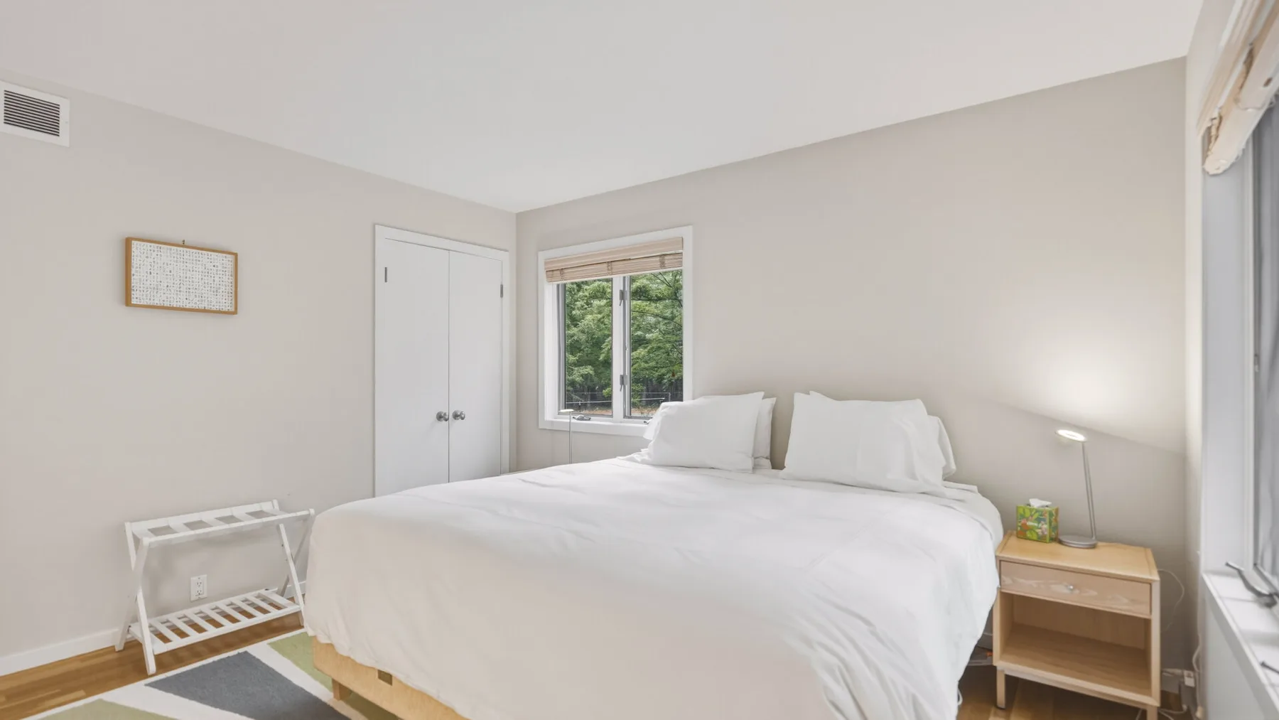 A bright bedroom with a neatly made bed beside a window and bedside table.