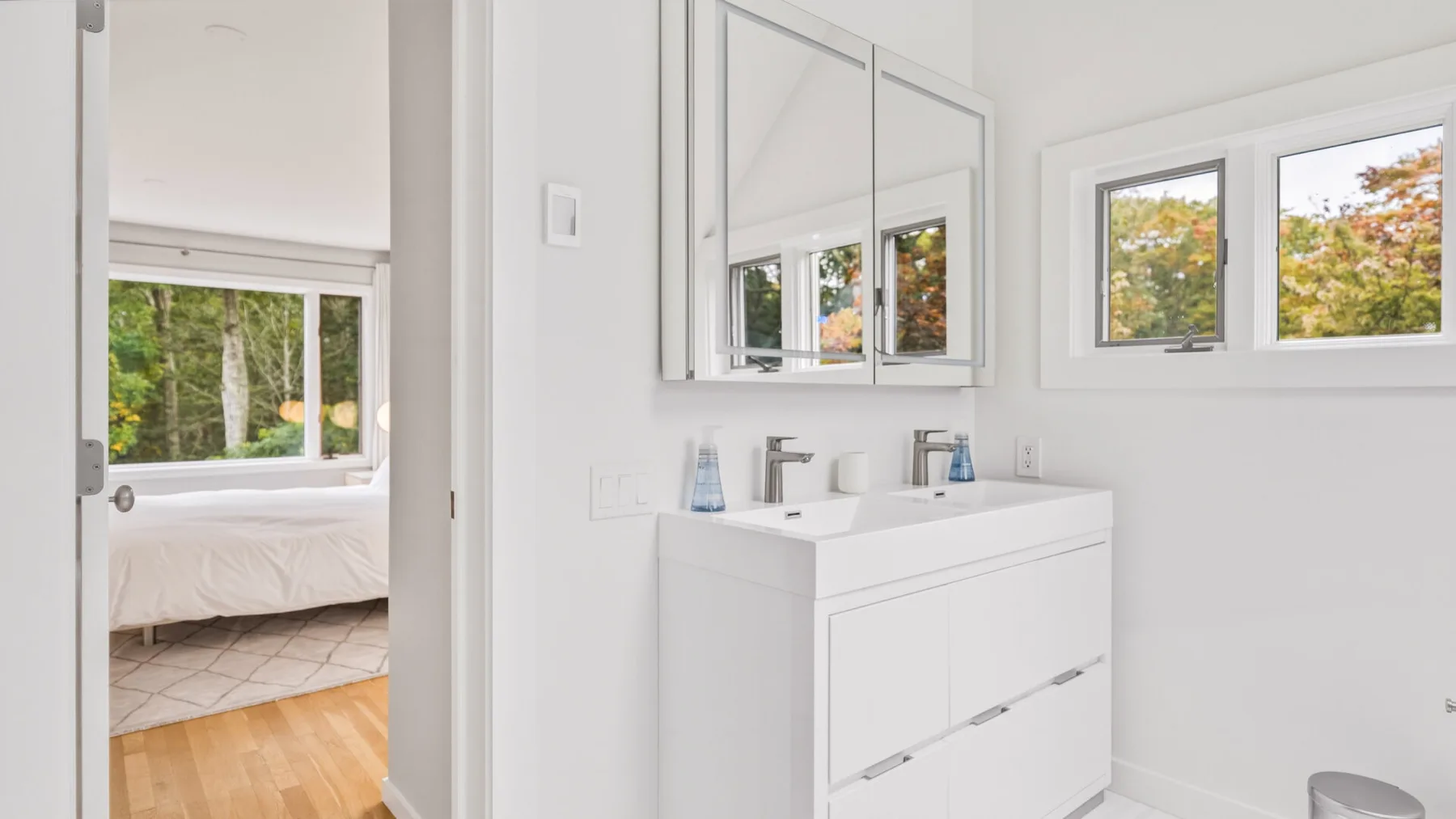 A bright bathroom with a white vanity and windows overlooking trees.