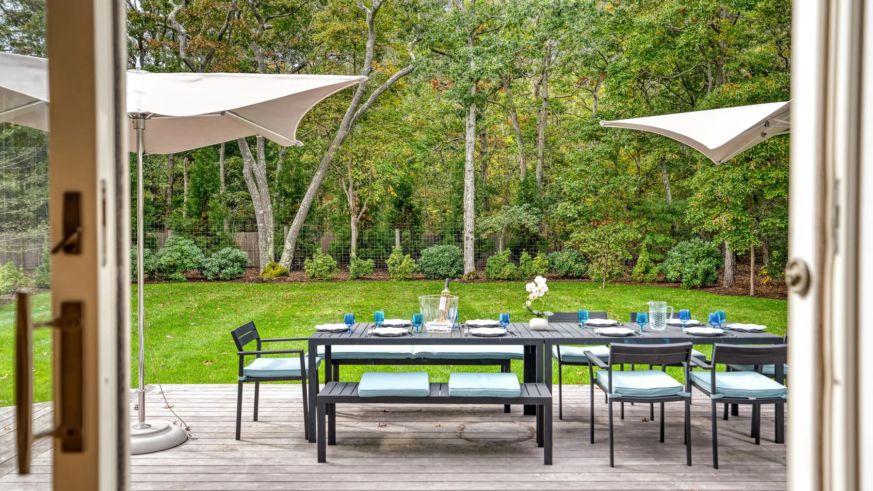 An outdoor dining area with a long table set on a patio beside a garden.