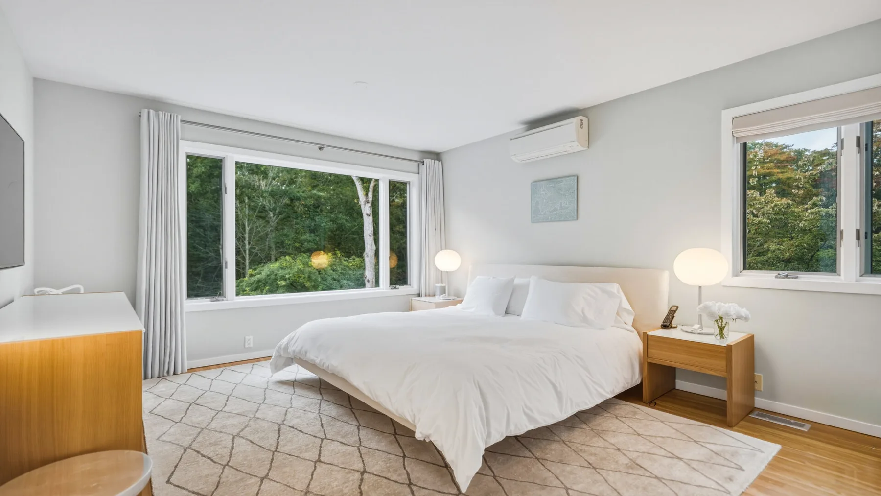 A bright bedroom with a white bed and large windows overlooking greenery.