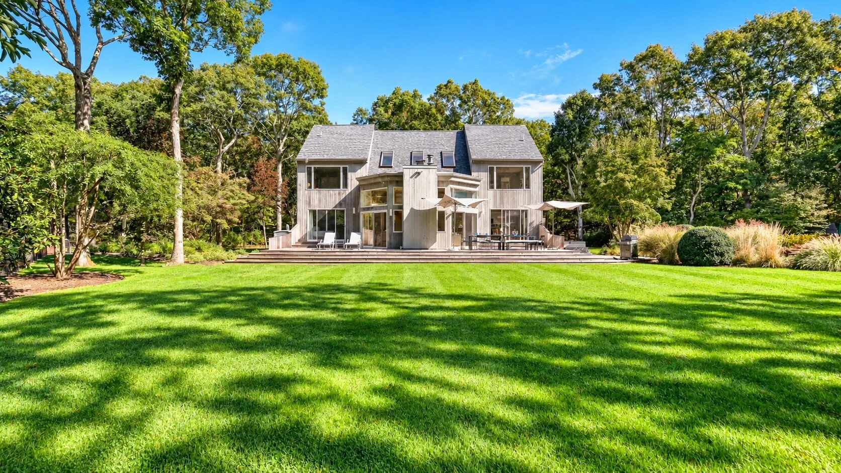A house with a broad green lawn and mature trees under a clear sky.