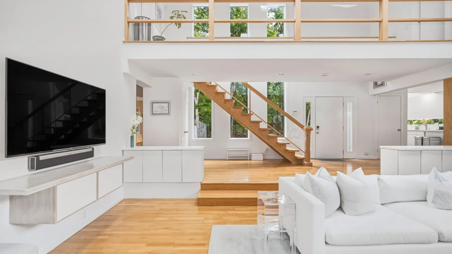 A bright open-plan living room with a white sofa and wooden staircase.