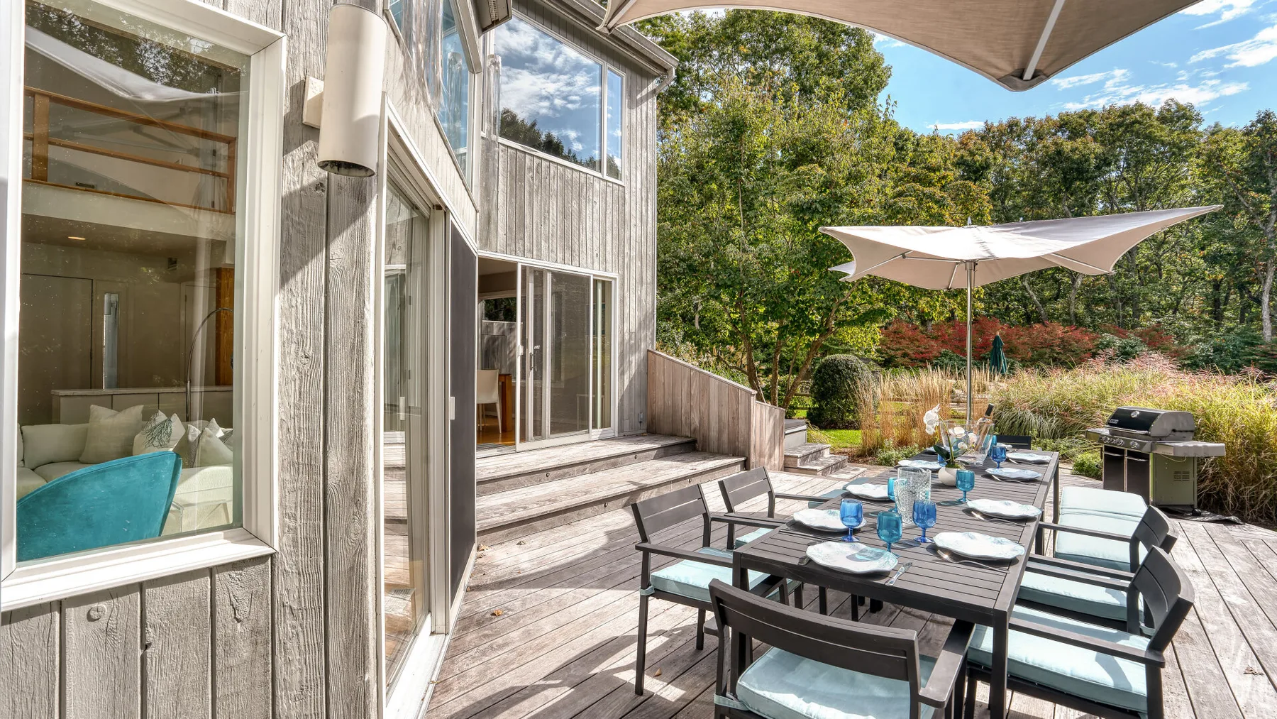 A wooden deck with outdoor dining furniture and large shade umbrellas beside the house.