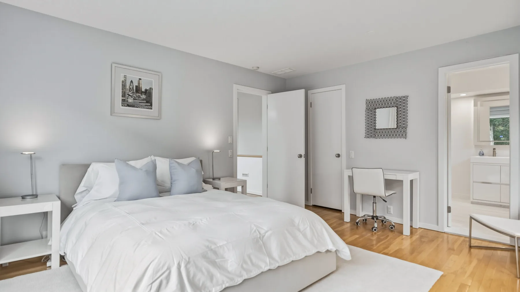 A bright bedroom with a large bed, bedside tables, and a doorway to an adjoining room.