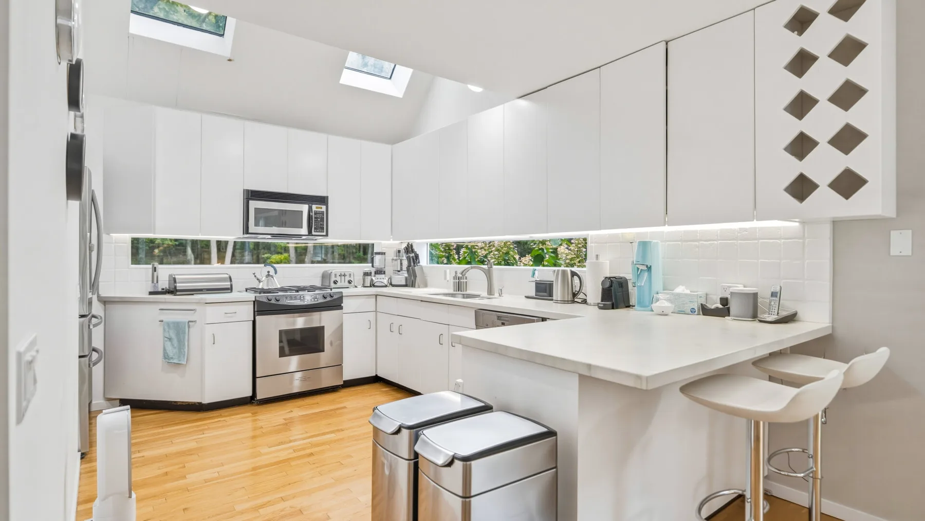 A bright kitchen with white cabinetry, stainless steel appliances, and a breakfast counter.