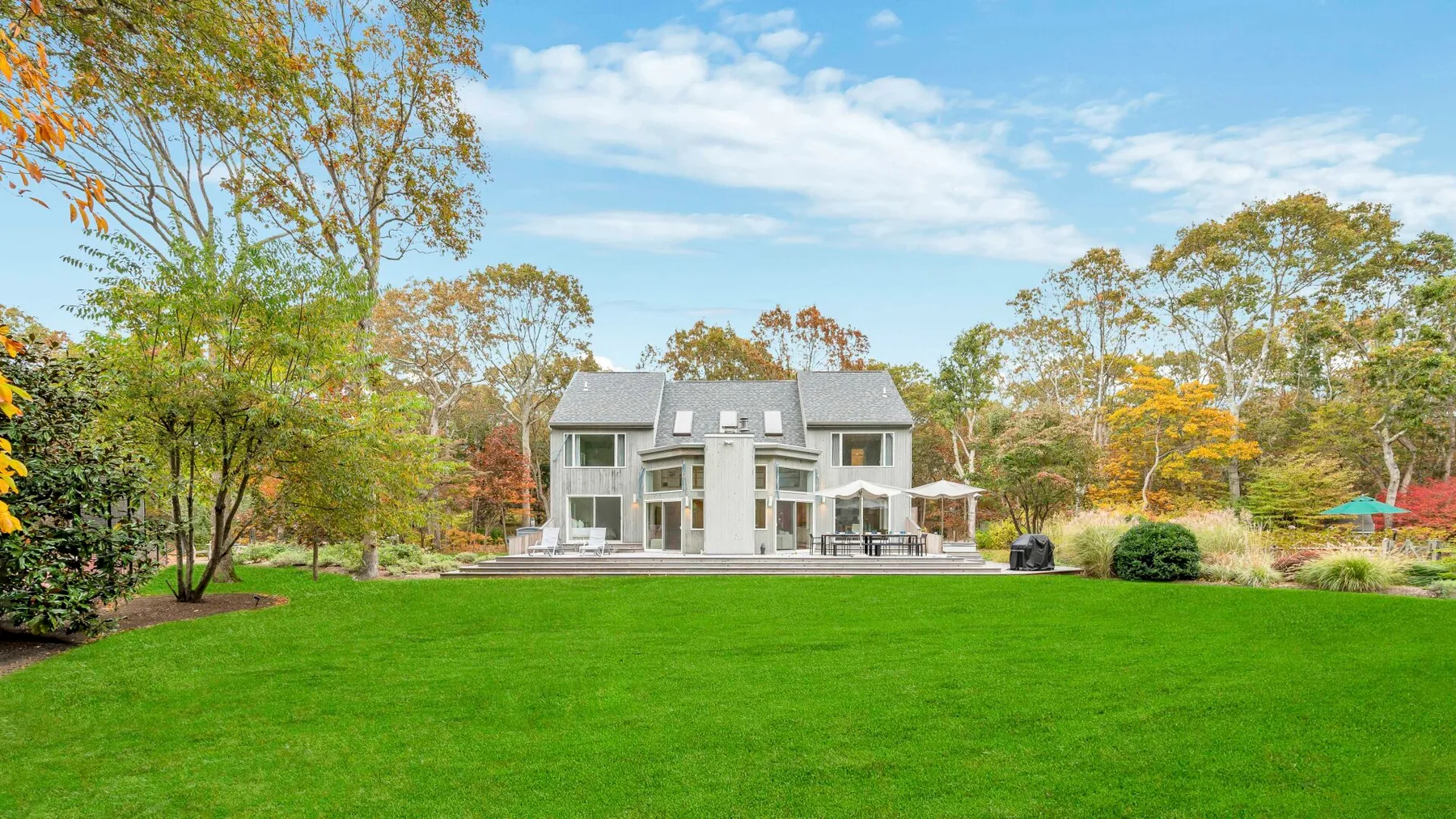 A large house stands beyond a broad green lawn, surrounded by trees.