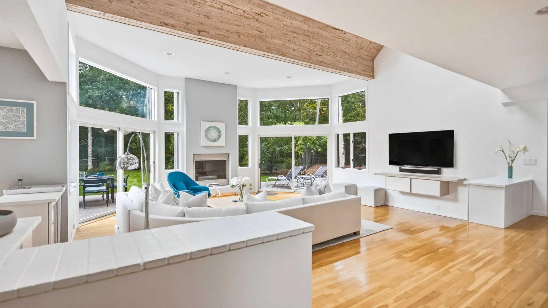 A bright living room with white seating, large windows, and a television.