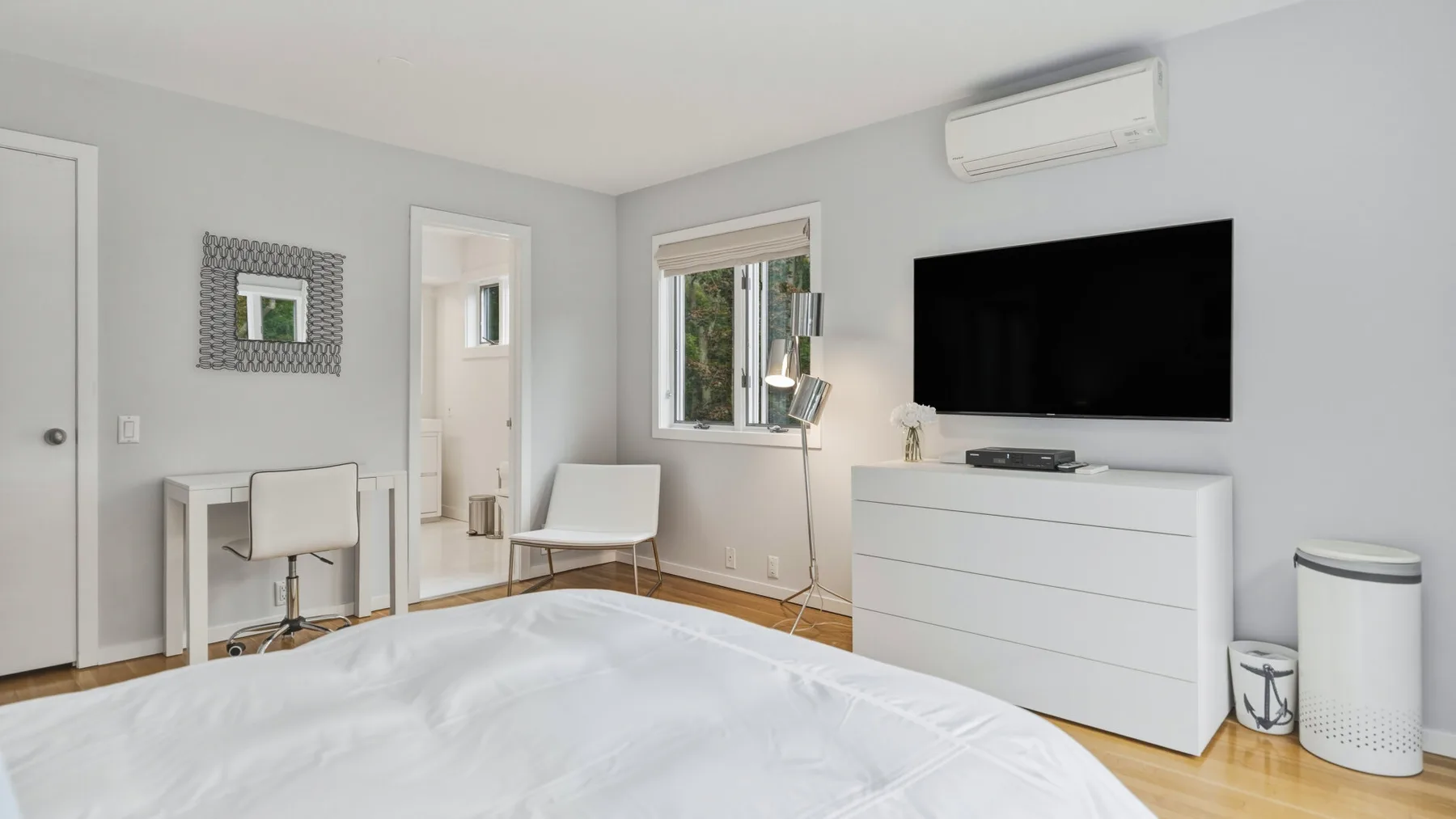 A bright bedroom with a bed, a wall-mounted television, and a white dresser.
