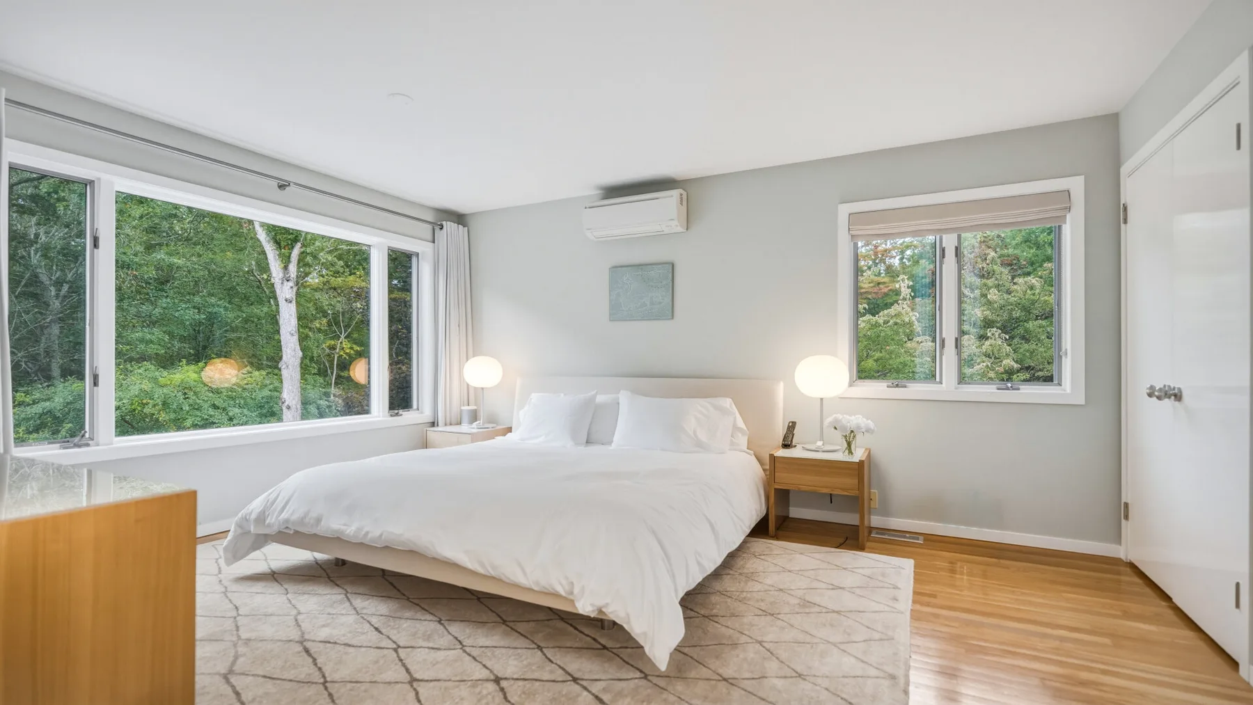A bright bedroom with a large bed, bedside tables, and windows overlooking greenery.