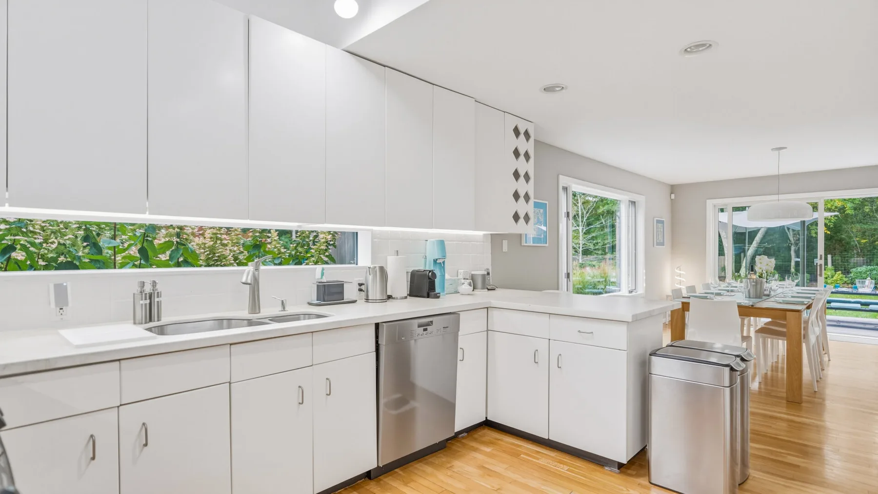 A bright kitchen with white cabinets, stainless steel appliances, and a wooden dining table.