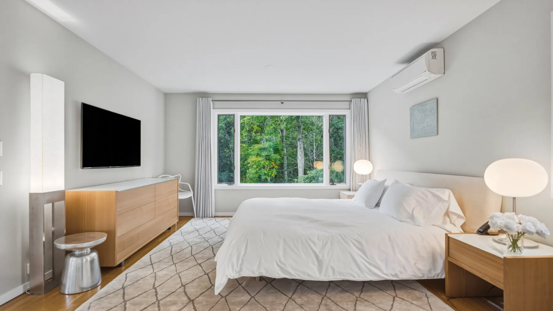 A bright bedroom with a large bed and a window overlooking greenery.