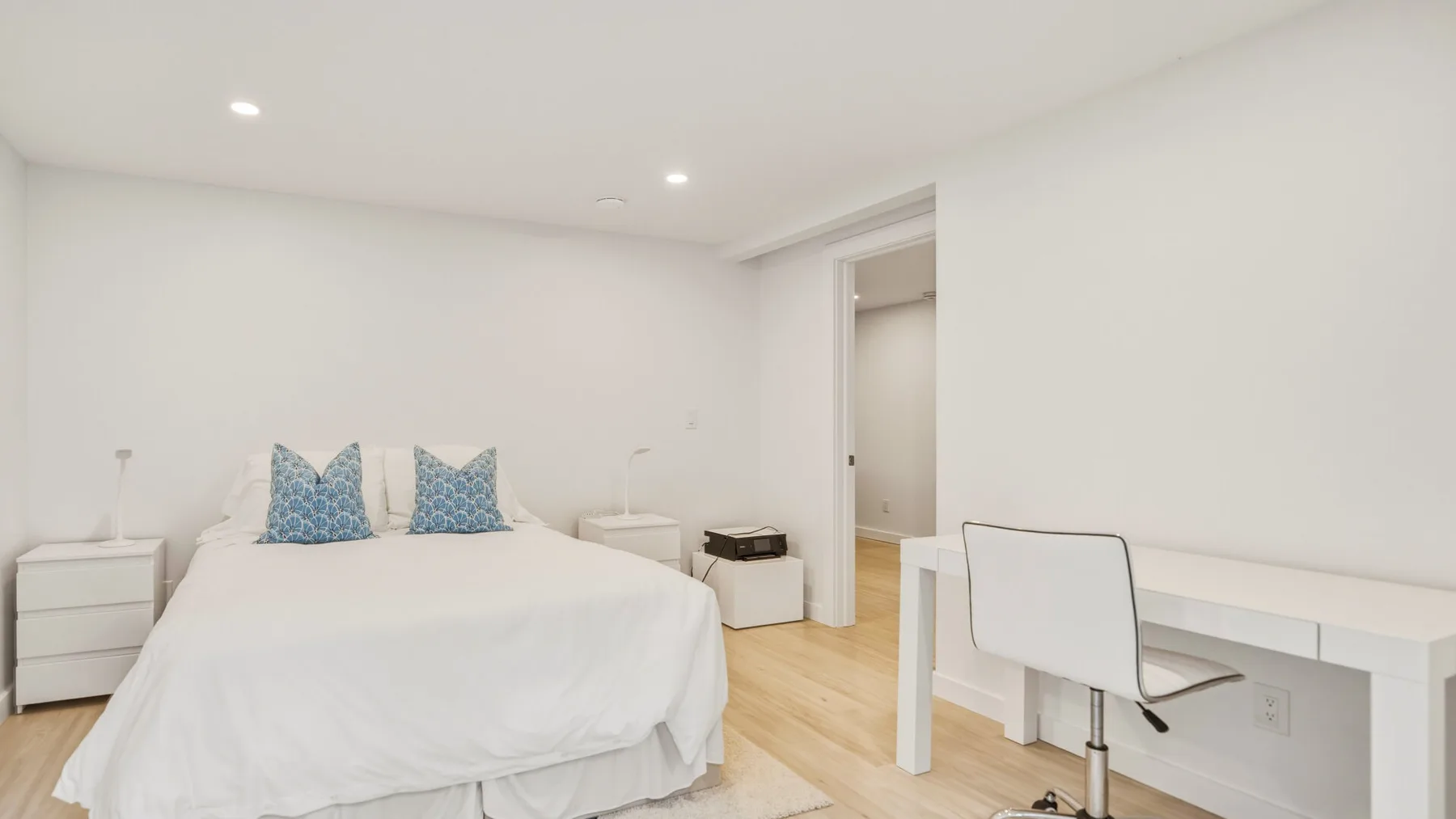 A bright bedroom with a bed and a desk beside the doorway.