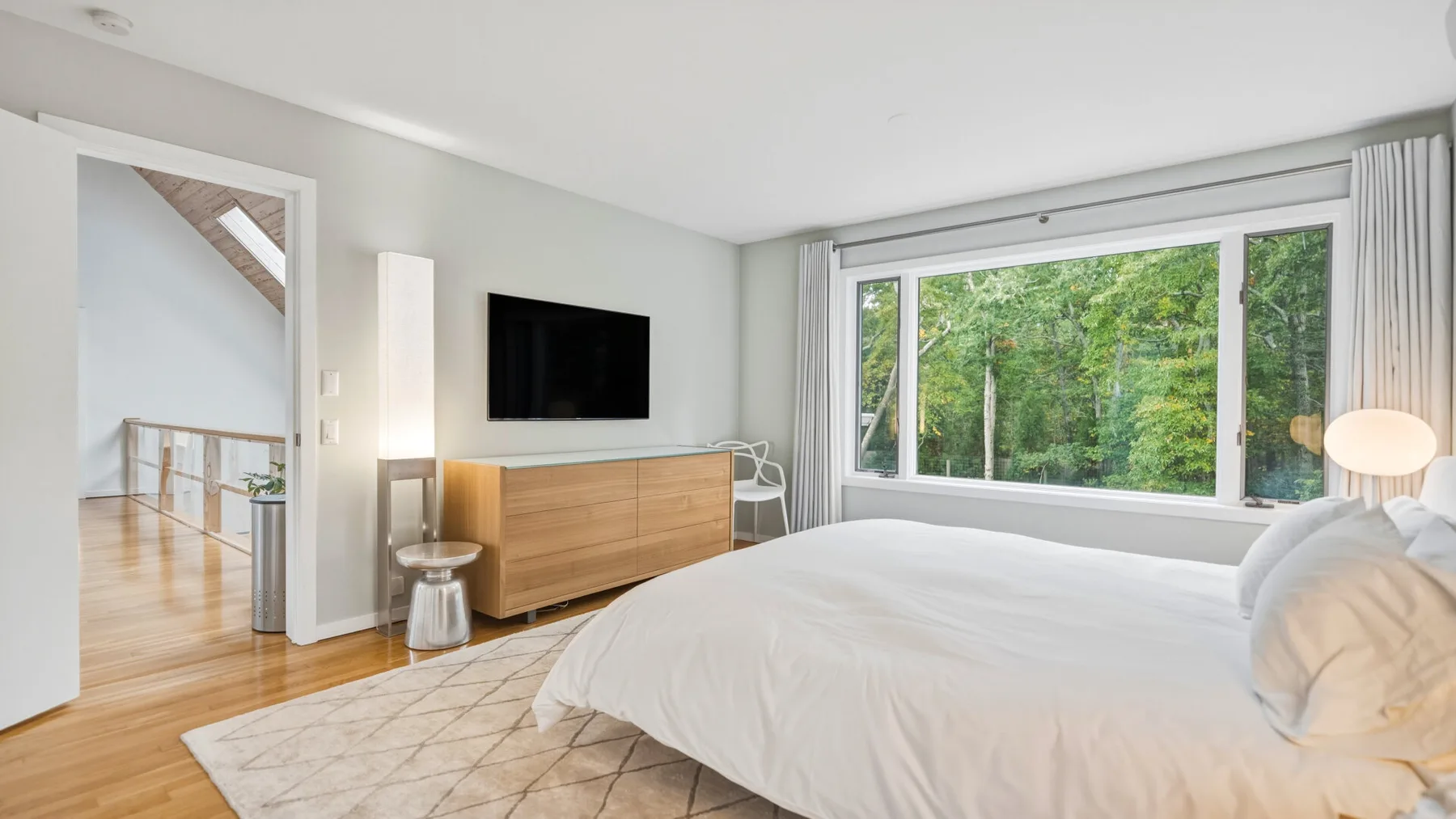 A bright bedroom with a large bed facing a wide window overlooking trees.