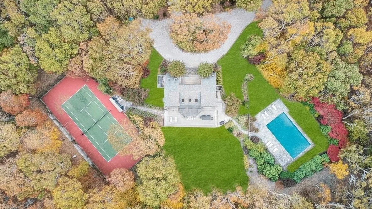An aerial view shows a landscaped property with a tennis court and swimming pool.