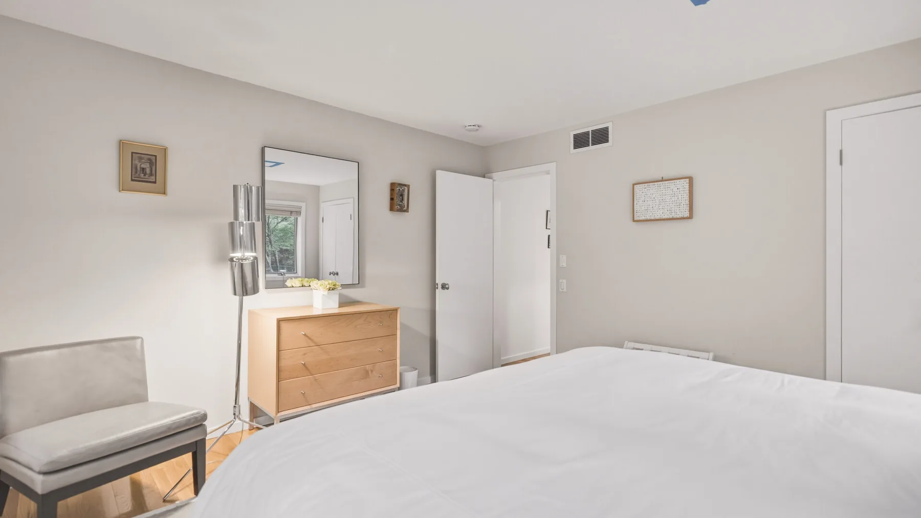A bright bedroom with a large bed, dresser, and wall mirror.