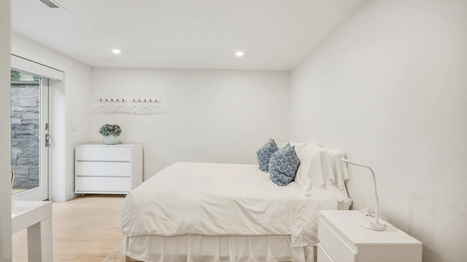 A bright bedroom with a white bed and bedside table.