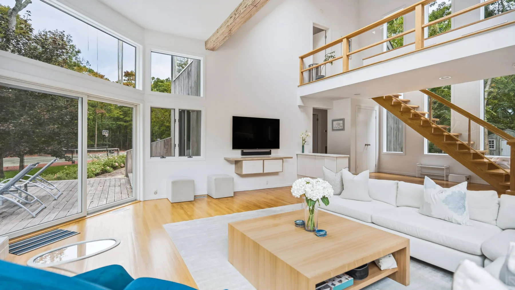 A bright living room with a white seating area, wooden coffee table, and staircase.
