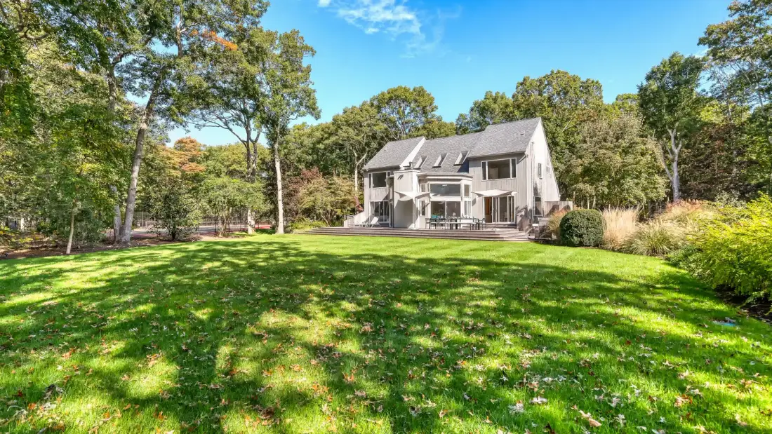 A house stands beyond a broad green lawn, with trees surrounding the yard.