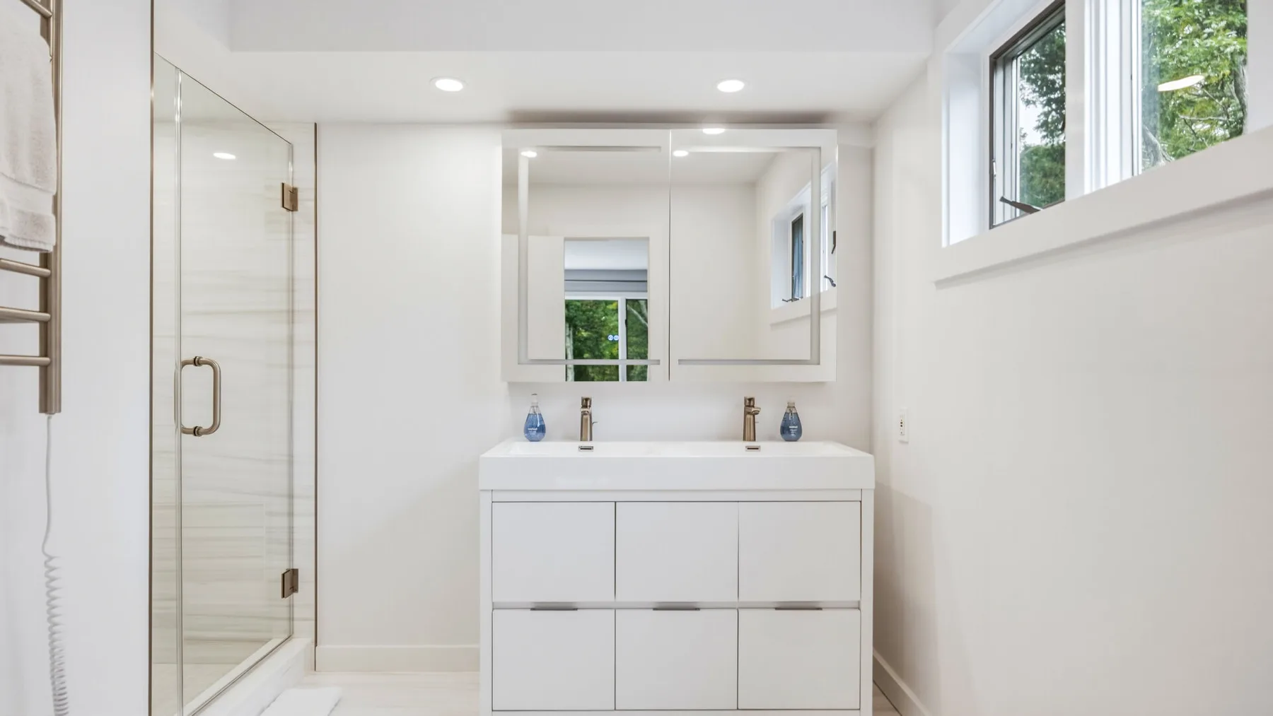 A bright bathroom with a wide vanity, mirror, and glass shower.