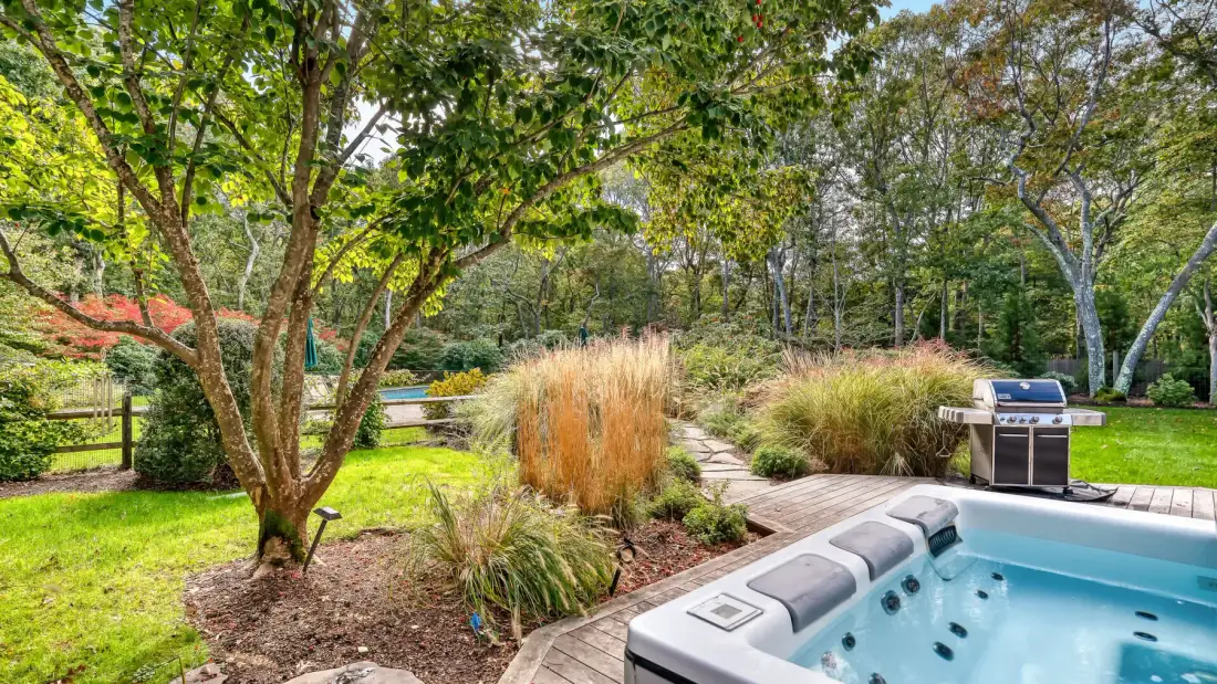 Un patio ajardinado con una bañera de hidromasaje y una parrilla exterior.