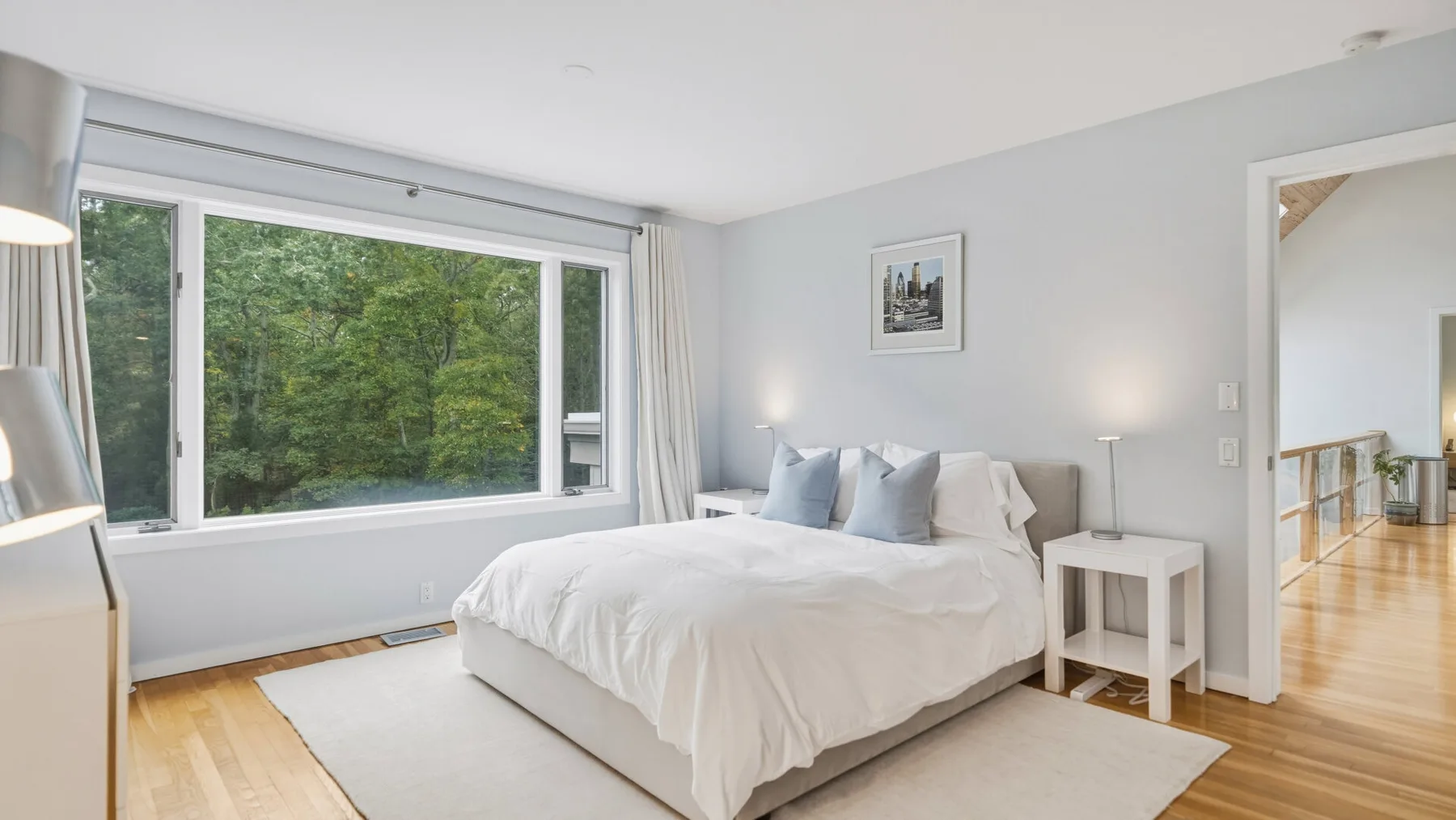 A bright bedroom with a bed beside a large window overlooking trees.