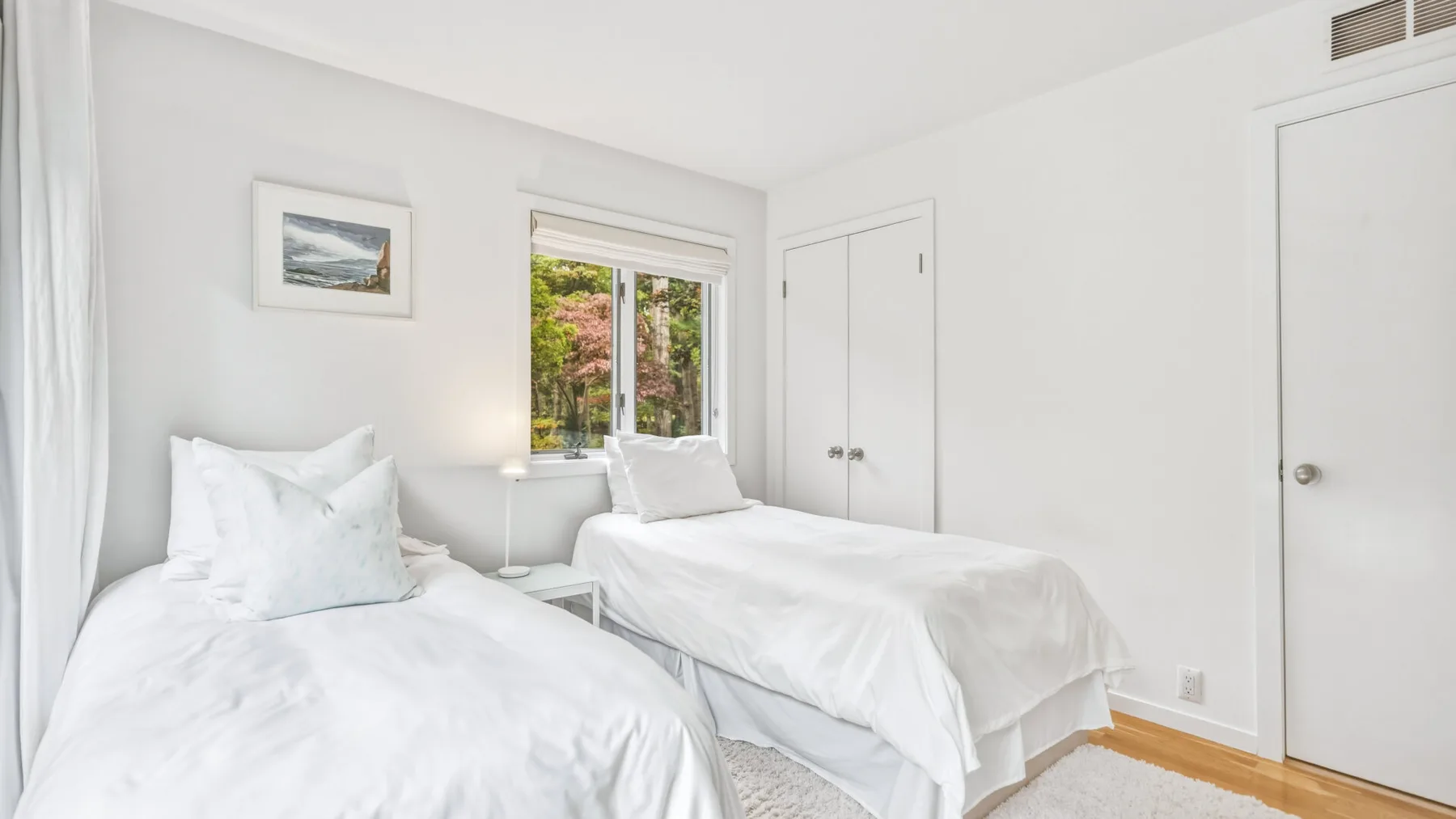A bright bedroom with two beds dressed in white linens.