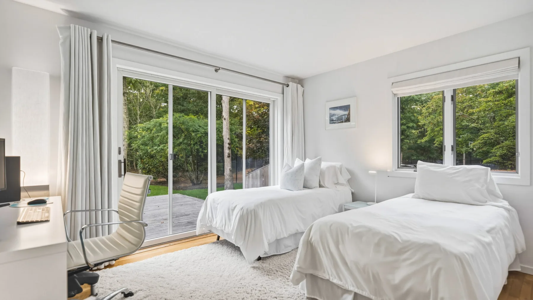 A bright bedroom with white bedding and large windows overlooking greenery.